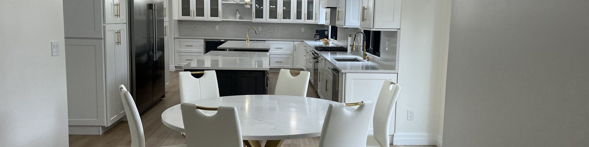 A white kitchen with a stone island and round stone table